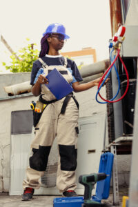 Adept repairman commissioned to optimize HVAC system efficacy, ensuring it operates at maximum capability. Proficient worker doing condenser unit investigation, imputing data on laptop
